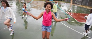 A young, cheerful girl jumping rope in the rain, surrounded by playing classmates